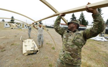 In this photo taken May 24, 2016, U.S. Army Spc. Dedric Bryant, right, of Fort Eustis in Newport News, Va., works to assemble temporary living structures at Joint Base Lewis-McChord in Washington state that will be used by troops taking part in a massive earthquake and tsunami readiness drill overseen by the Federal Emergency Management Agency on June 7-10, 2016. (AP Photo/Ted S. Warren)