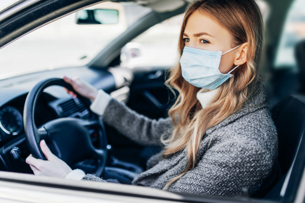 Beautiful young girl in a mask sitting in a car, protective mask
