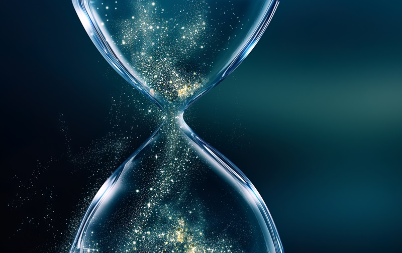 Glass hourglass on dark background with glowing sand