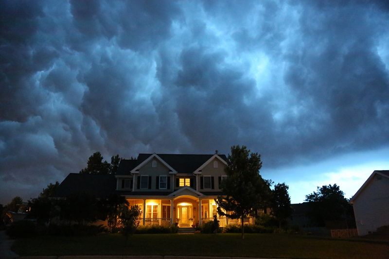 A well appointed house is lit up while a large thunderstorm moves in overhead.