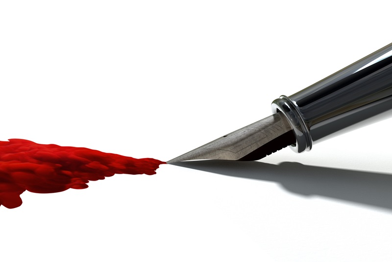 A side view of the metal nib of an old fountain pen jetting out a stream of thick red ink on an isolated white background